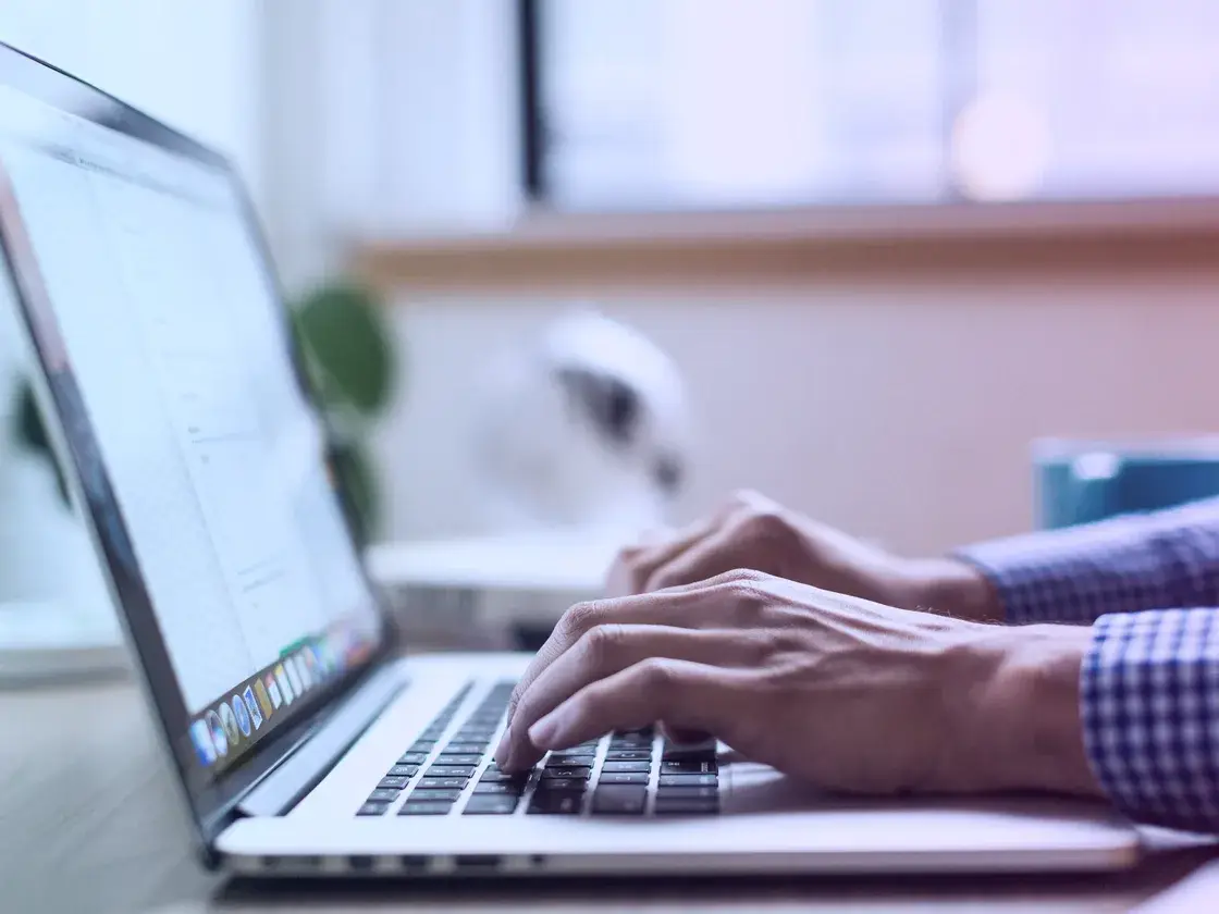 Hands typing on a laptop at a bright workspace
